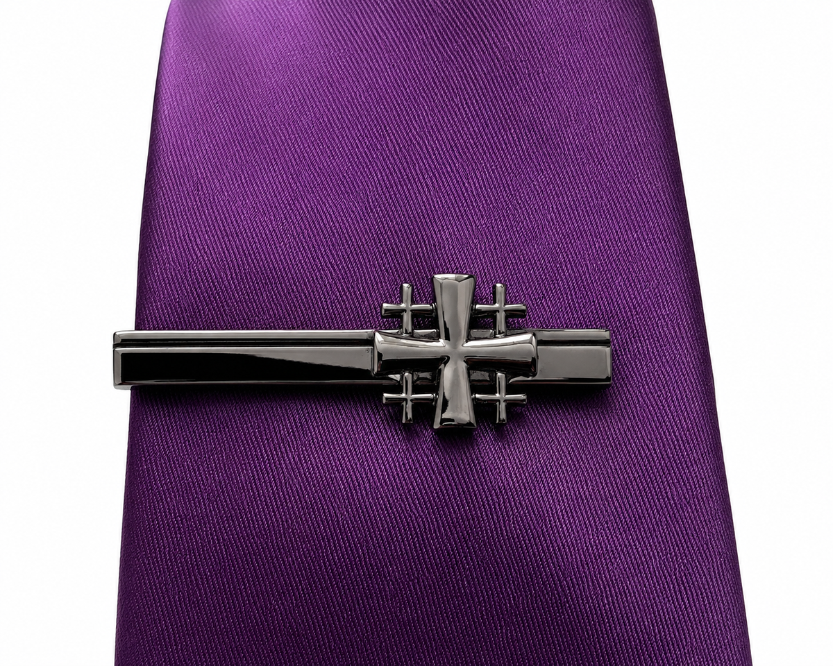A silver-toned tie bar with a Gunmetal Jerusalem Cross Tie Clip cross design, shown clipped to a purple textured necktie on a white background.