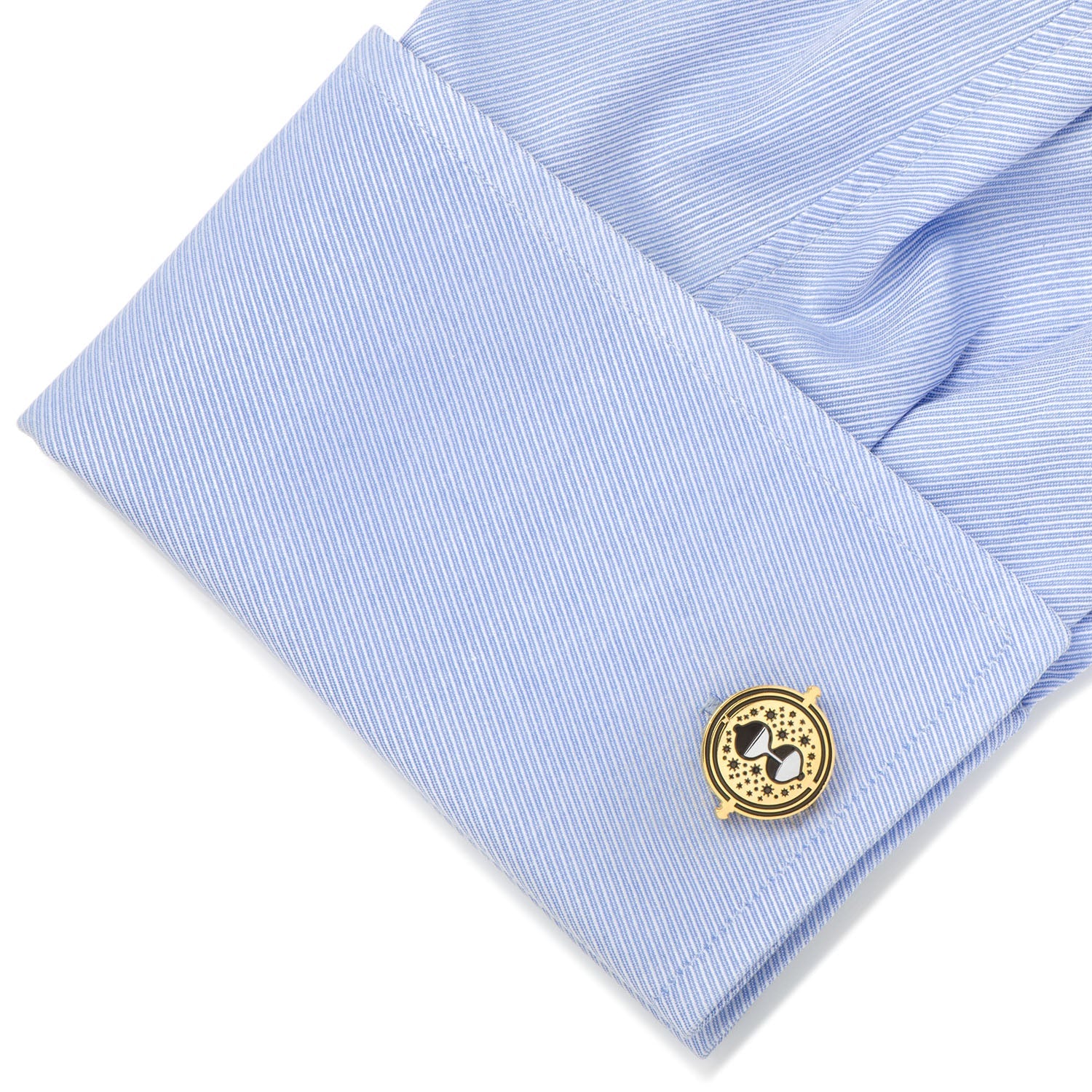 Gold cufflink on a light blue dress shirt with a white background