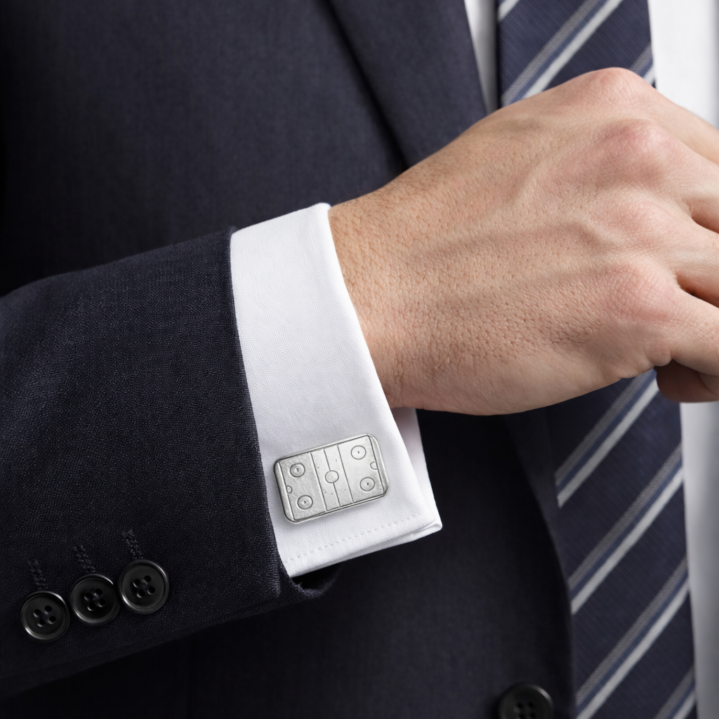 Close-up of a person wearing a dark suit with a white shirt and striped tie, focusing on the cufflink.