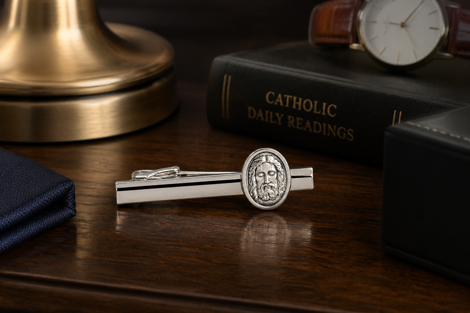 Silver tie clip with religious design on a wooden surface with books and a watch.