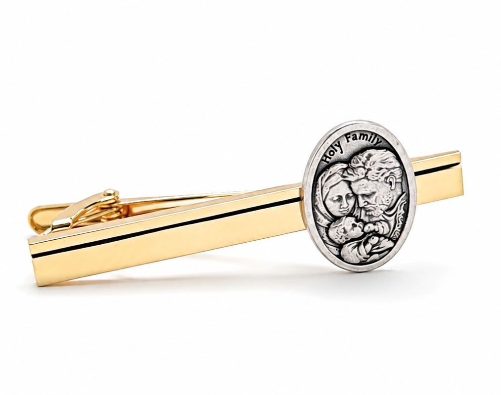A gold and silver tie clip featuring a polished gold bar with a thin black stripe and a round silver-toned medallion engraved with a religious figure and the text 'Holy Family