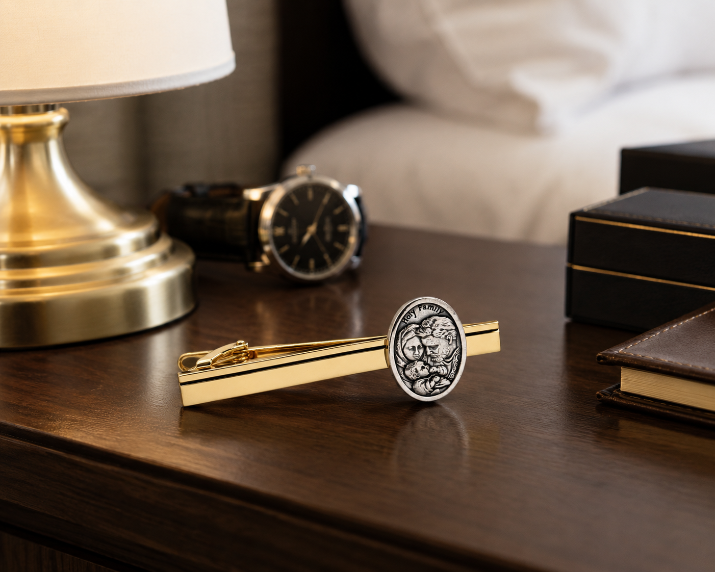 A gold tie bar with a circular silver-toned lion emblem, resting on a dark wooden bedside table next to a watch, lamp, and boxes.
