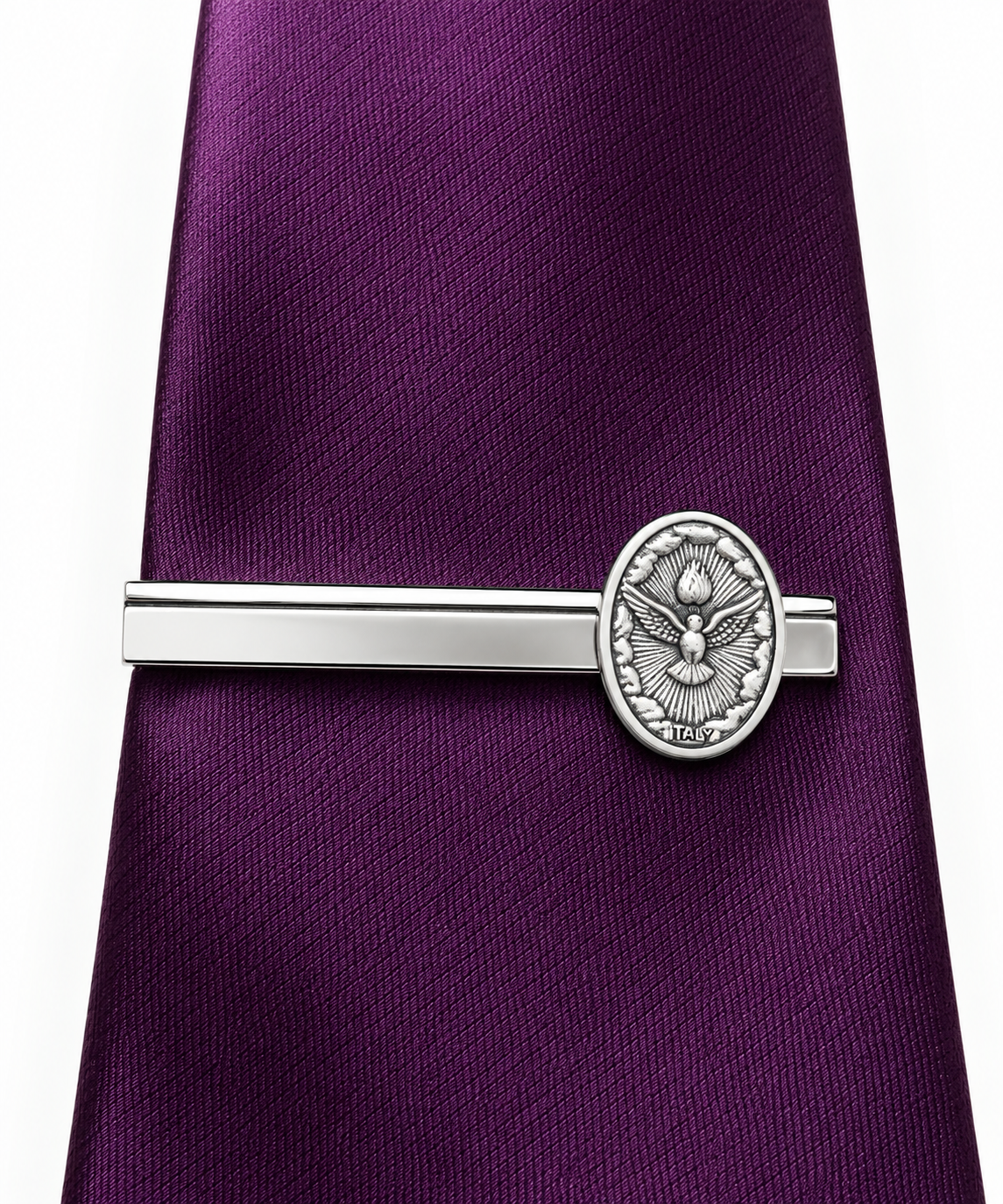 A silver tie clip with an embossed eagle emblem, shown fastening a purple silk tie against a white background.