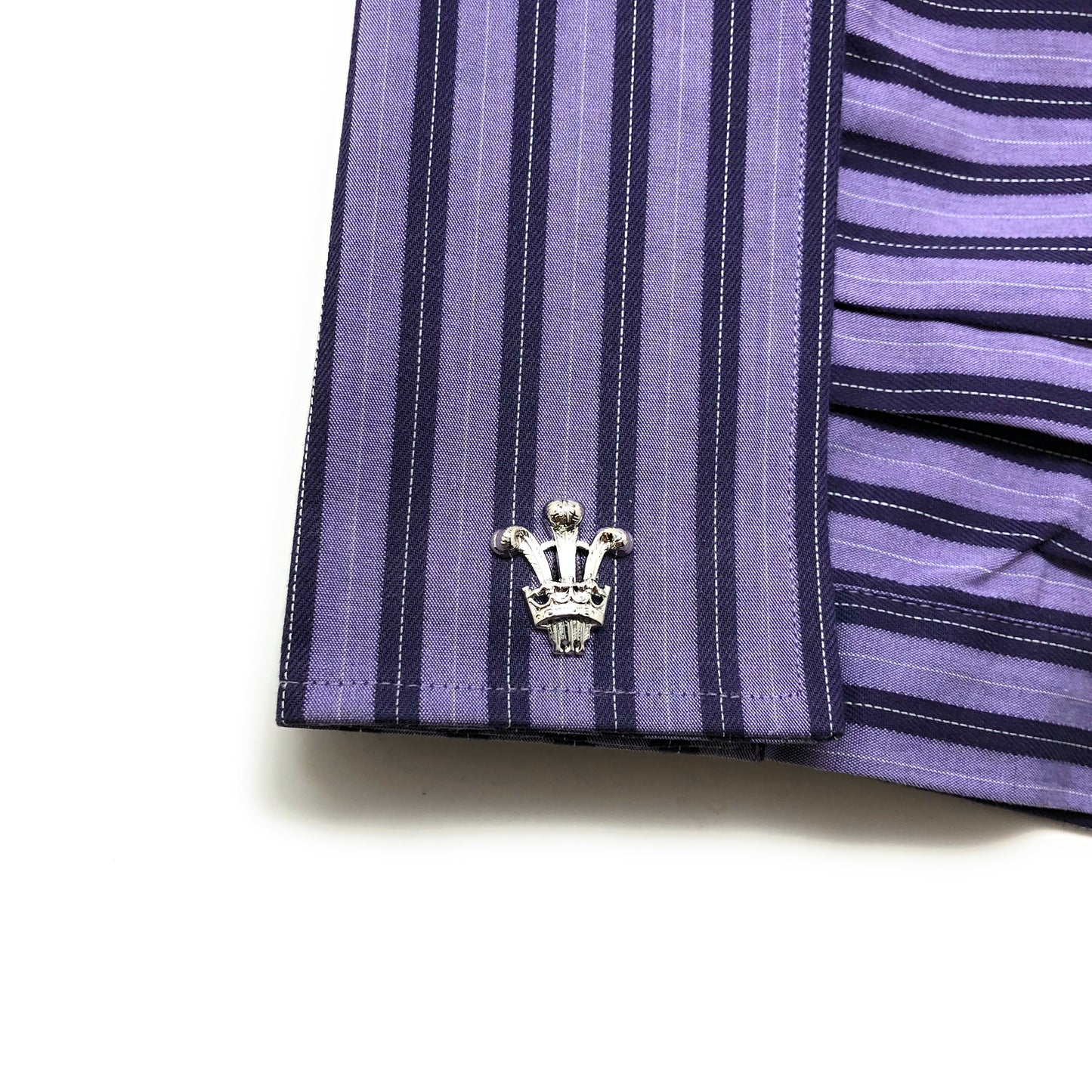 Close-up of a purple and black striped shirt with a decorative button on a white background Silver Prince of Wales cufflinks featuring the classic three-feather royal emblem – luxury men’s accessories from JayPins