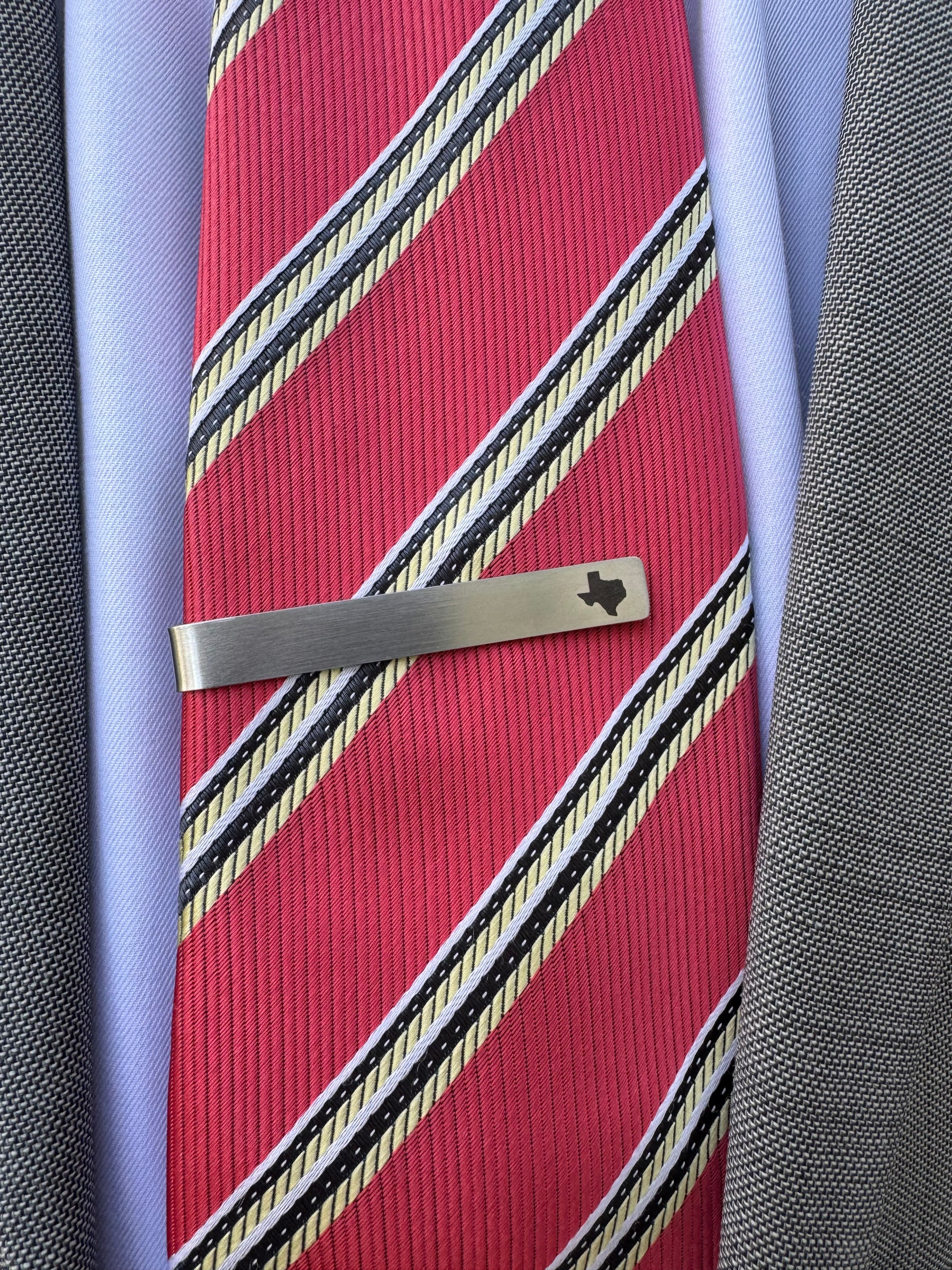 Red striped tie with a silver tie clip on a textured surface