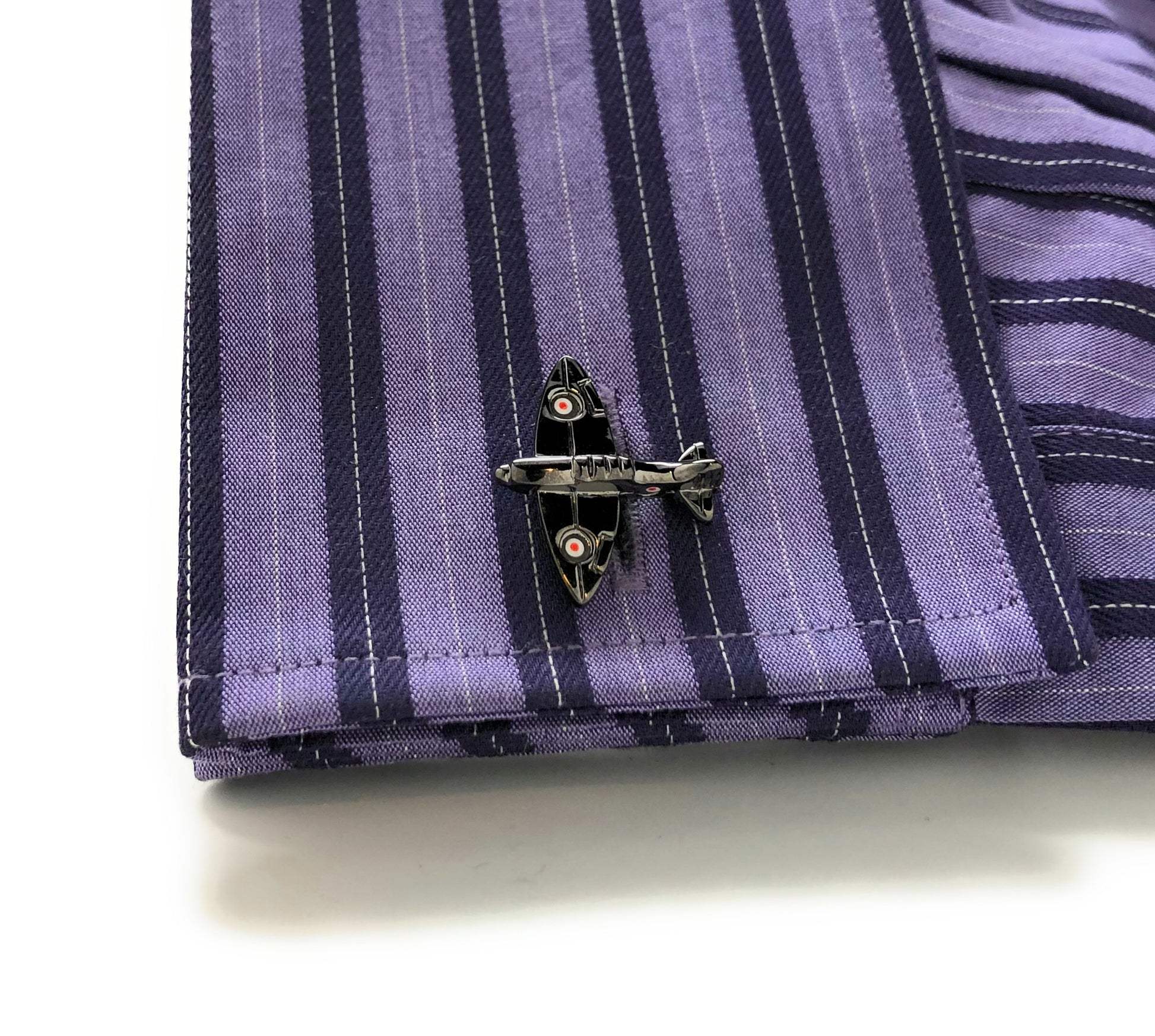 Close-up of a purple striped shirt with a black airplane cufflink on a white background