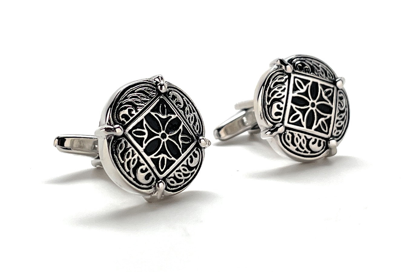 Pair of silver cufflinks with intricate black designs on a white background