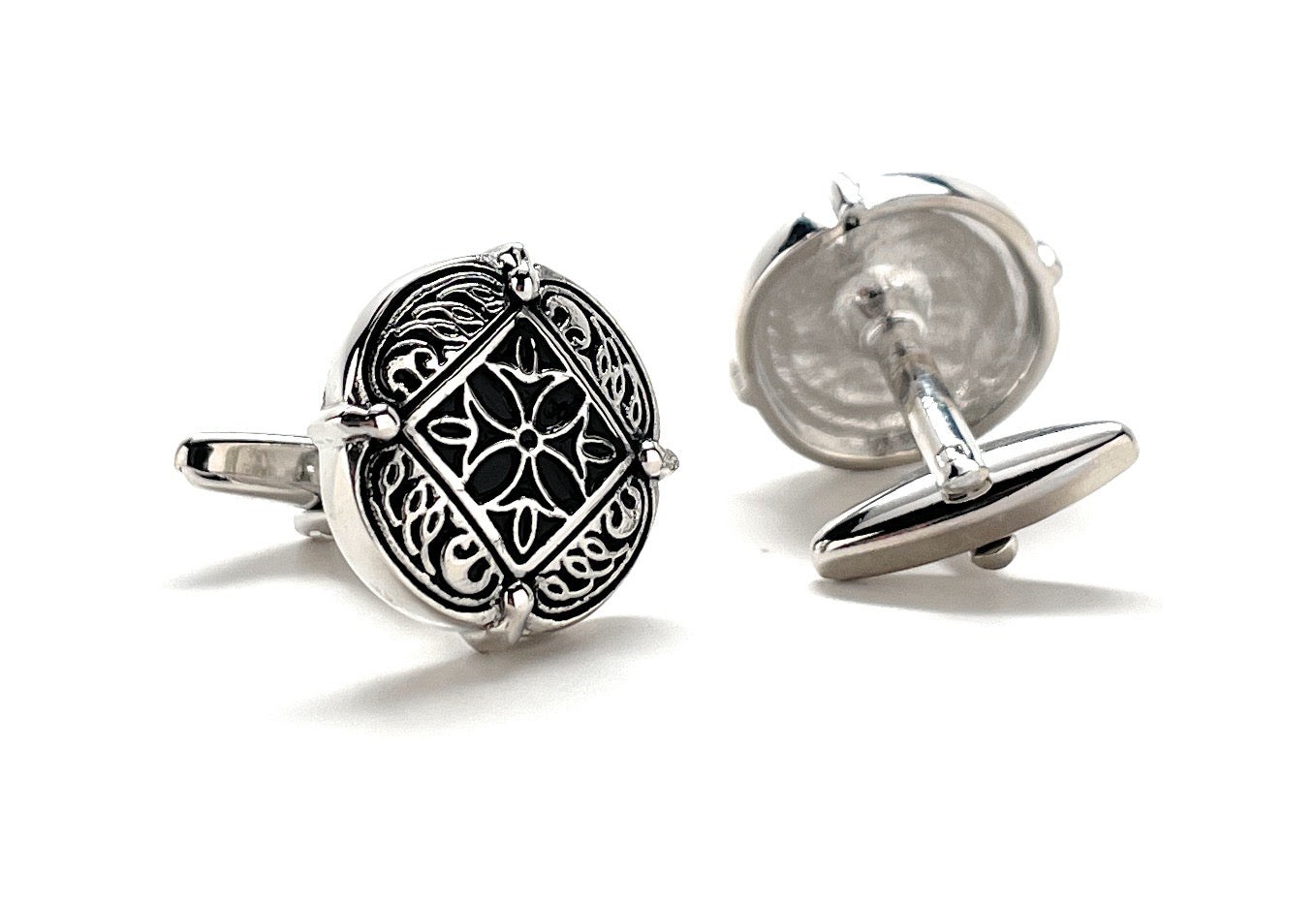 Silver cufflinks with intricate design on a white background