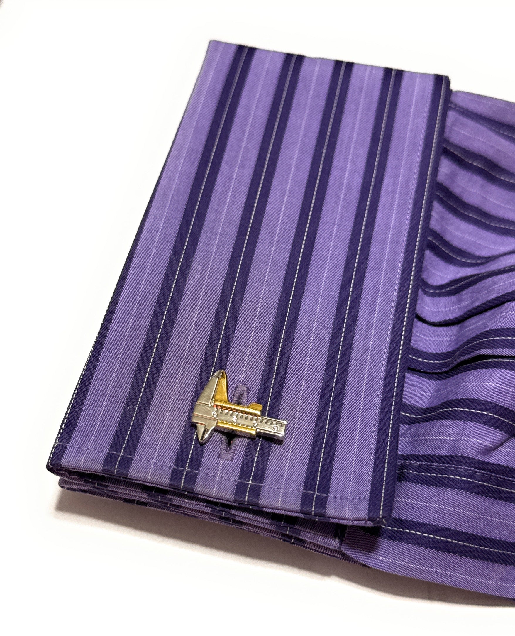 Purple striped pocket square with a gold and black lapel pin on a white background