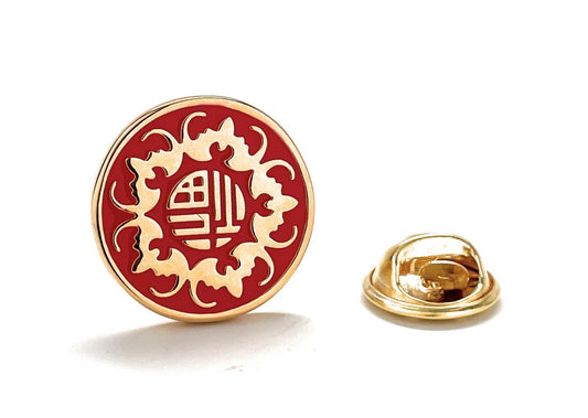 Red and gold lapel pin with intricate design on a white background