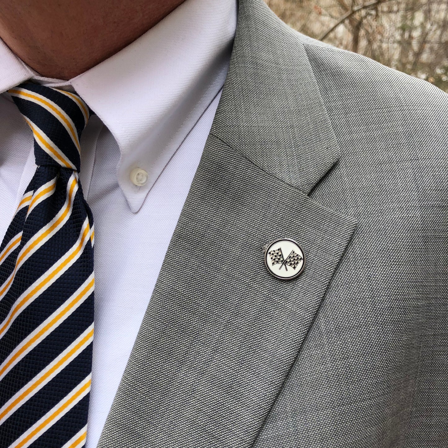 Checkered flag lapel pin displayed on a suit jacket – crossed flags racing pin accessory for motorsport fans and NASCAR enthusiasts.