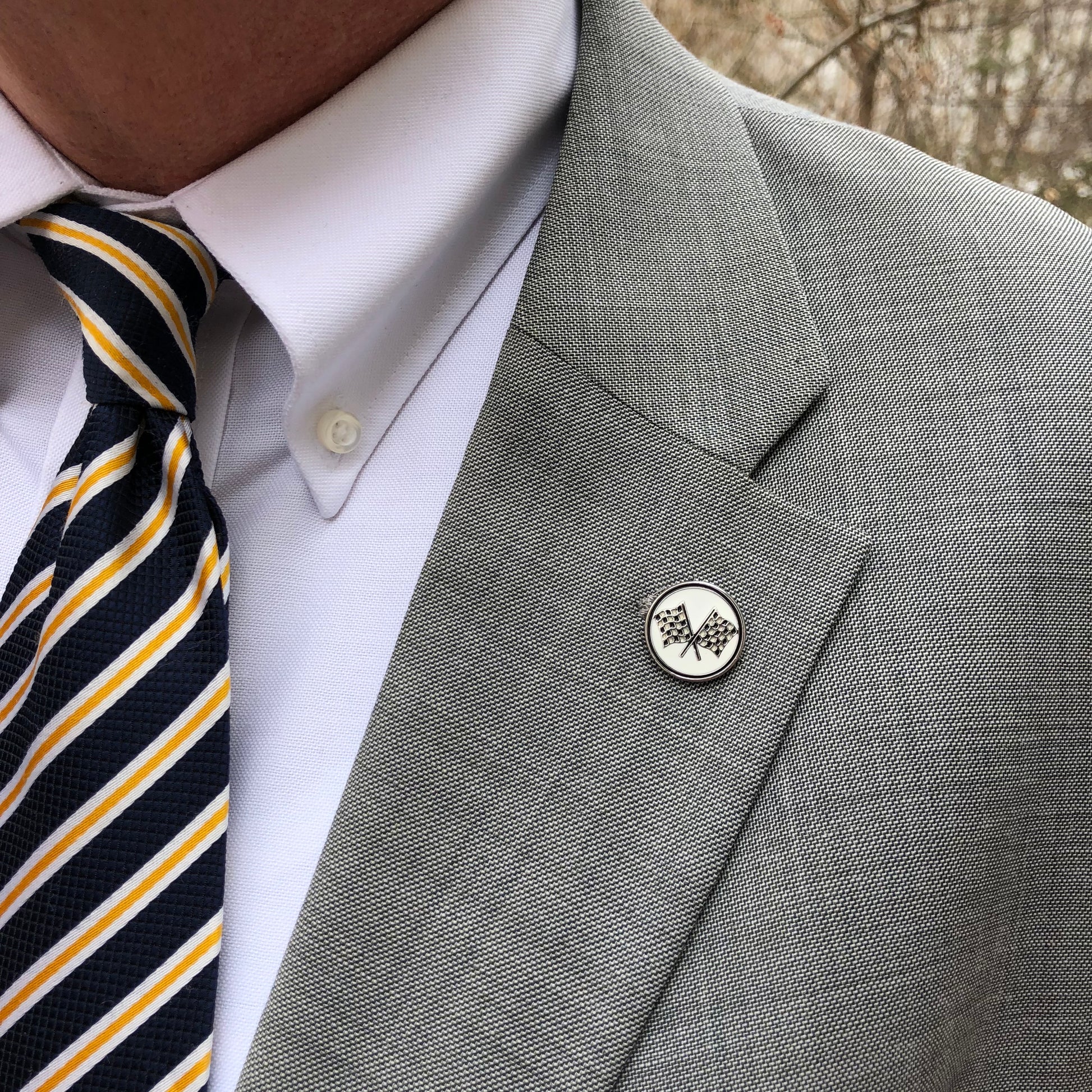 Checkered flag lapel pin displayed on a suit jacket – crossed flags racing pin accessory for motorsport fans and NASCAR enthusiasts.