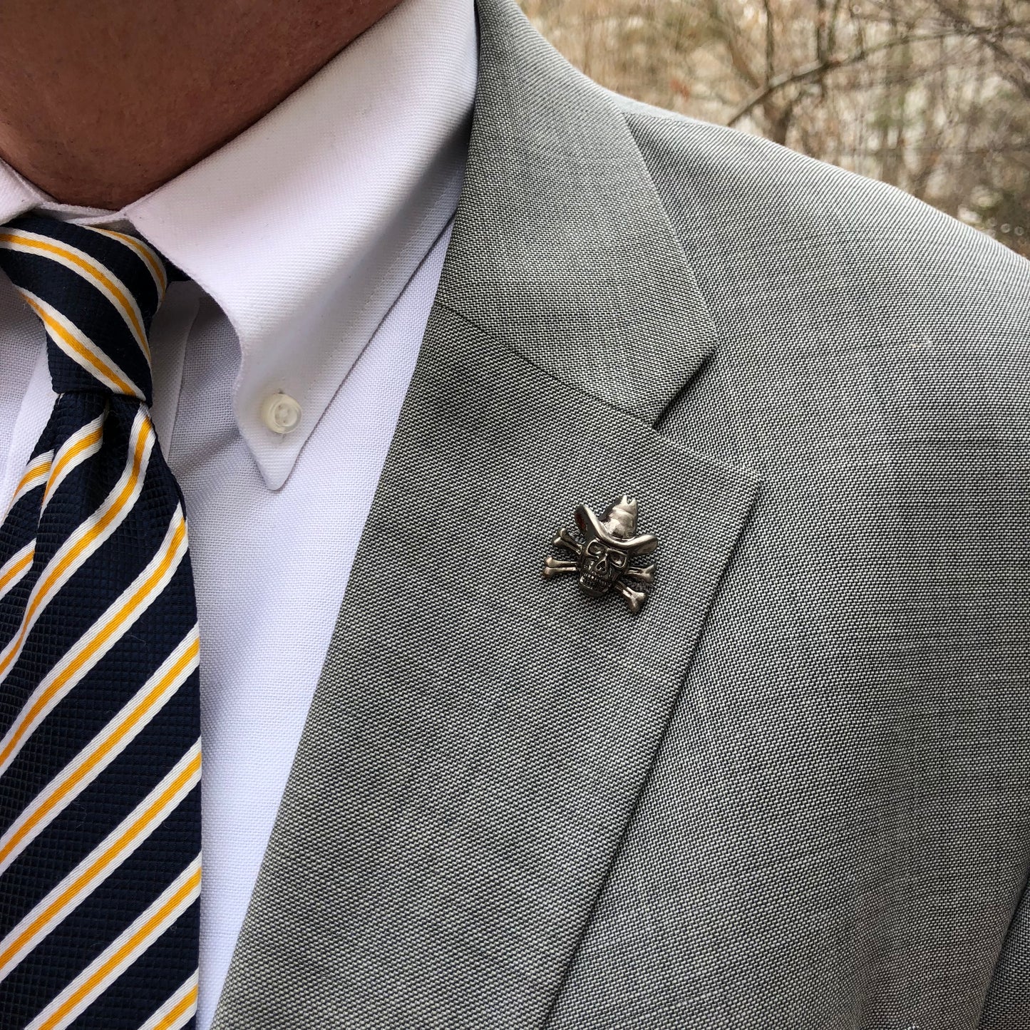 Gray suit jacket with a decorative pin, white shirt, and striped tie.