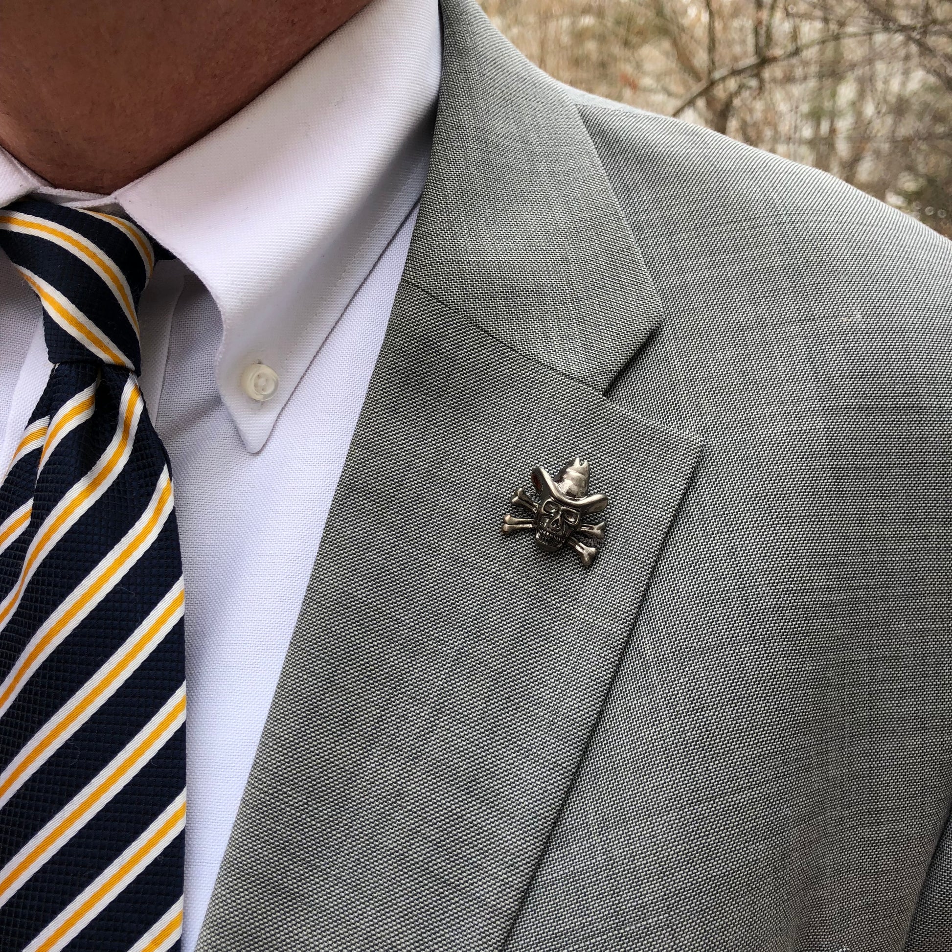 Gray suit jacket with a decorative pin, white shirt, and striped tie.