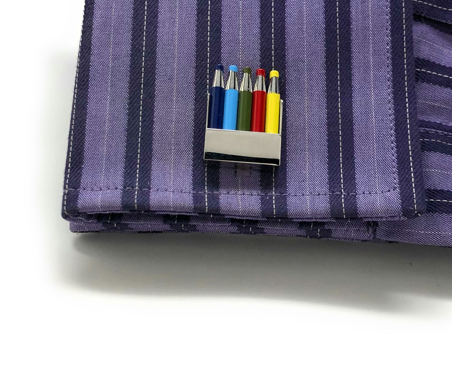 Purple striped fabric with a small metallic clip holding colorful markers.