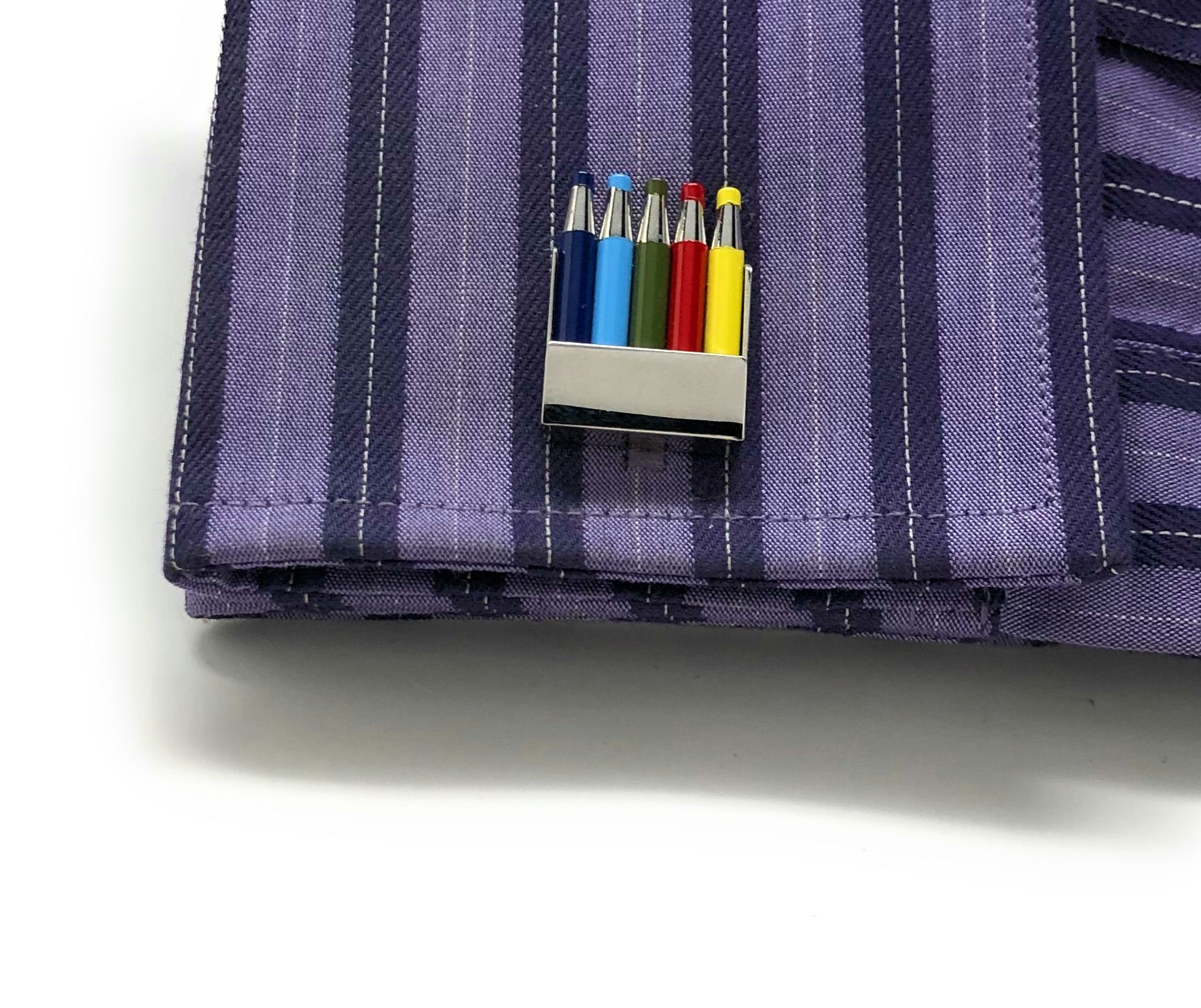 Purple striped fabric with a small metallic clip holding colorful markers.