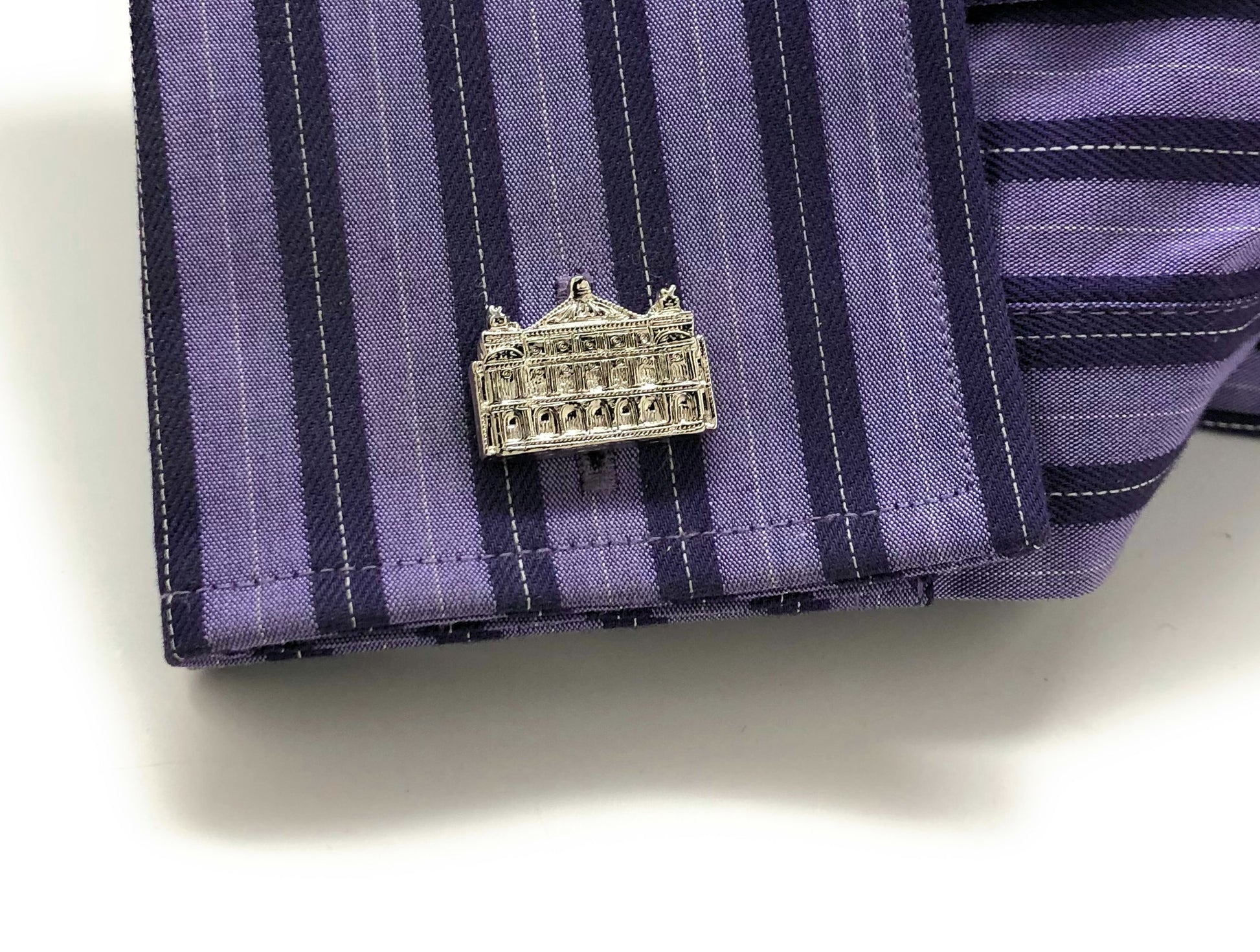 Silver building-shaped pin on a purple striped fabric background