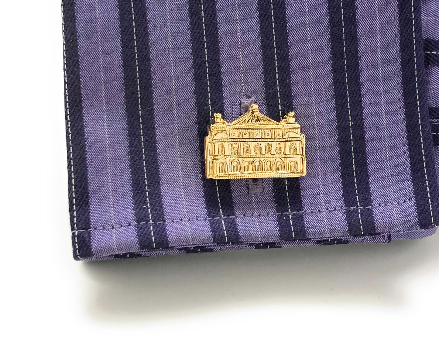 Gold building-shaped pin on a purple striped fabric background