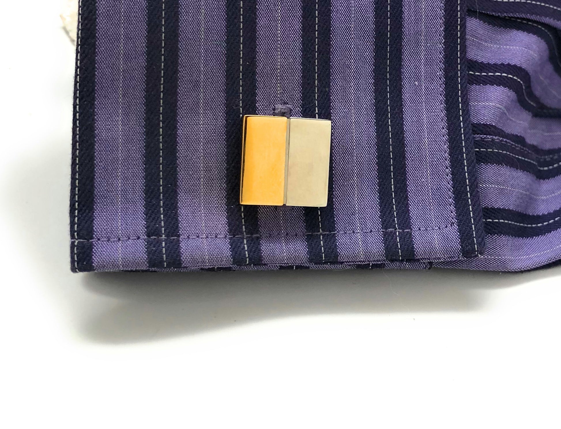 Close-up of a purple striped fabric with a yellow and beige tag on a white background
