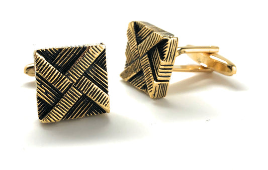 Two gold and black geometric cufflinks on a white background