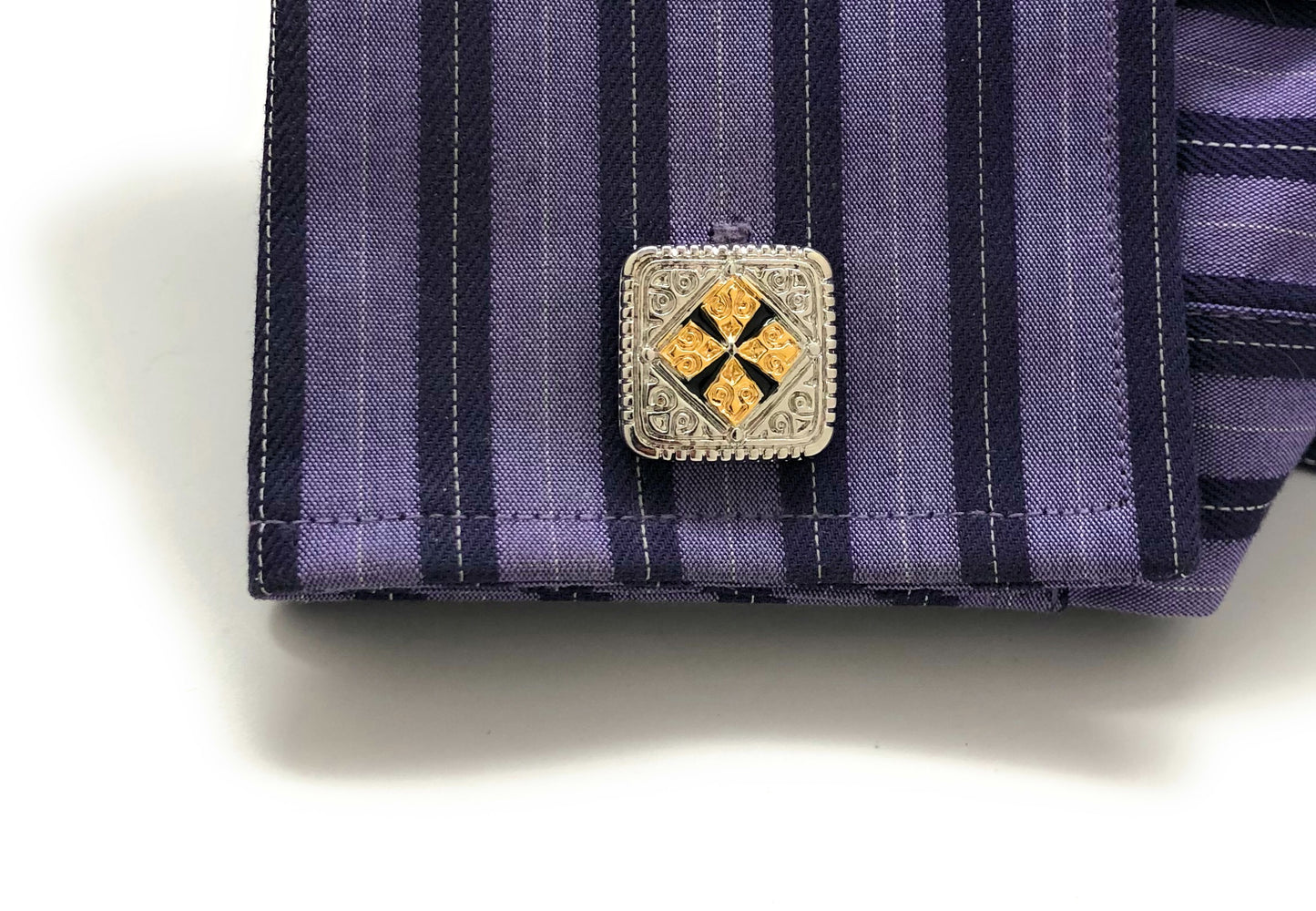 Close-up of a purple striped shirt with a decorative cufflink on a white background