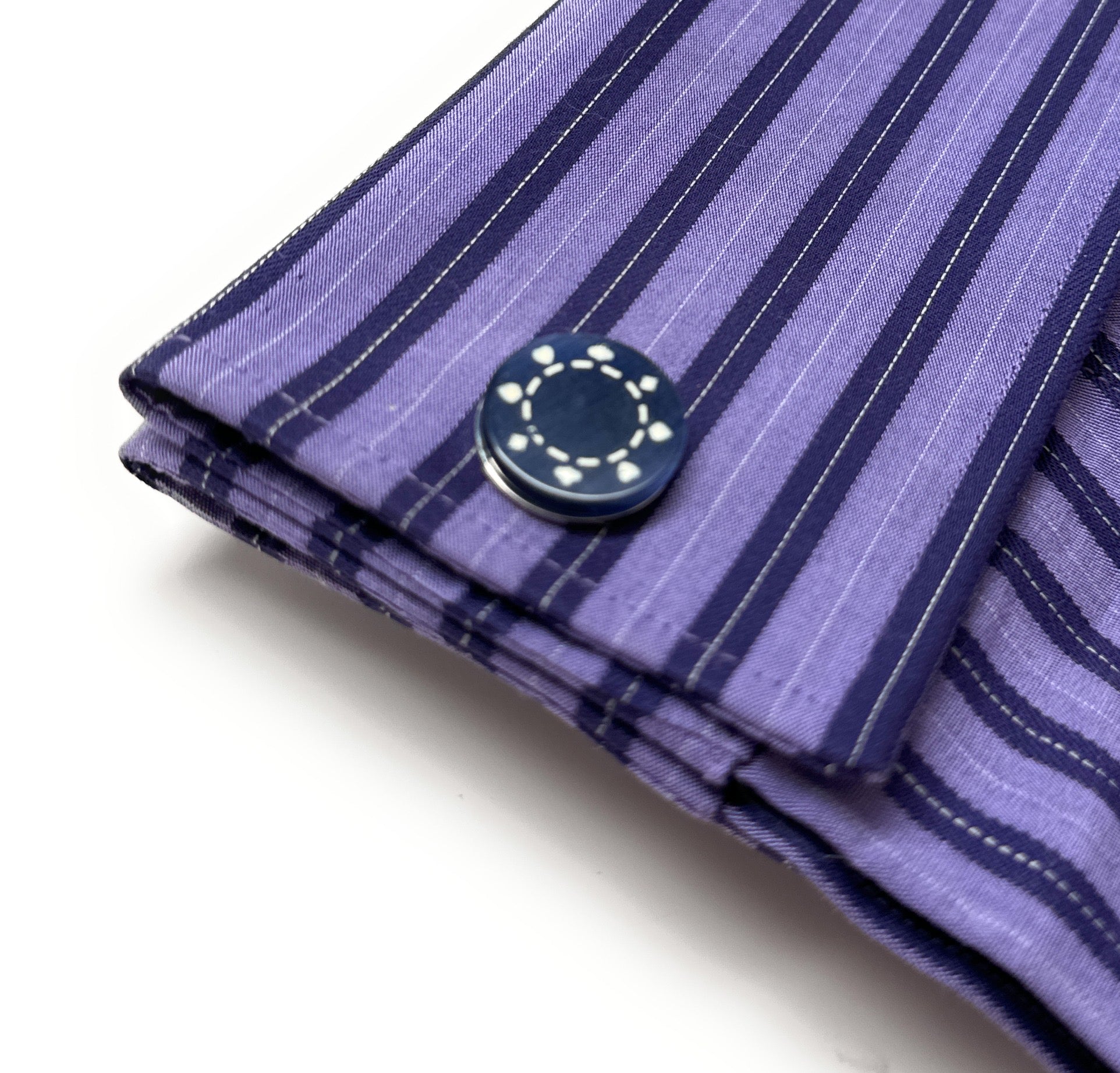 Close-up of a purple striped shirt cuff with a button on a white background