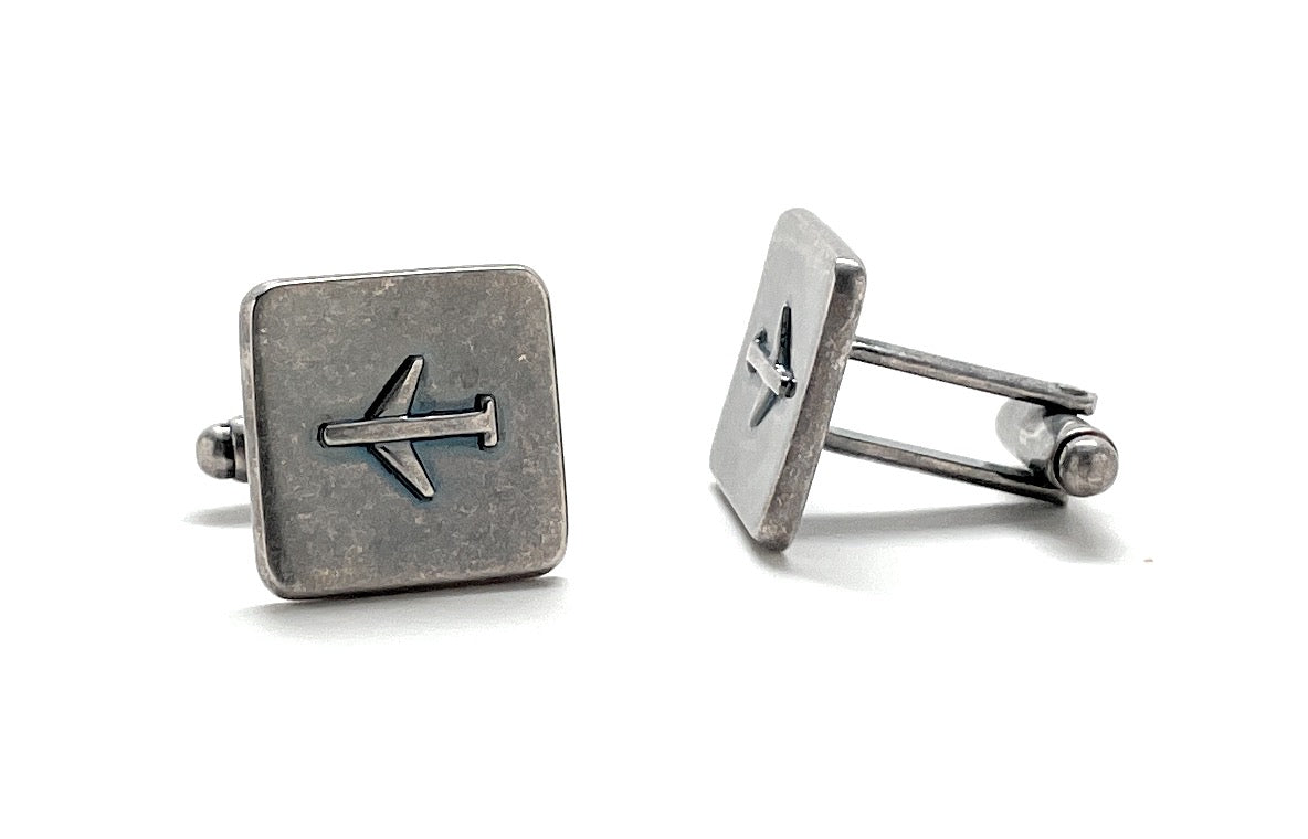 Pair of silver cufflinks with airplane symbol on a white background