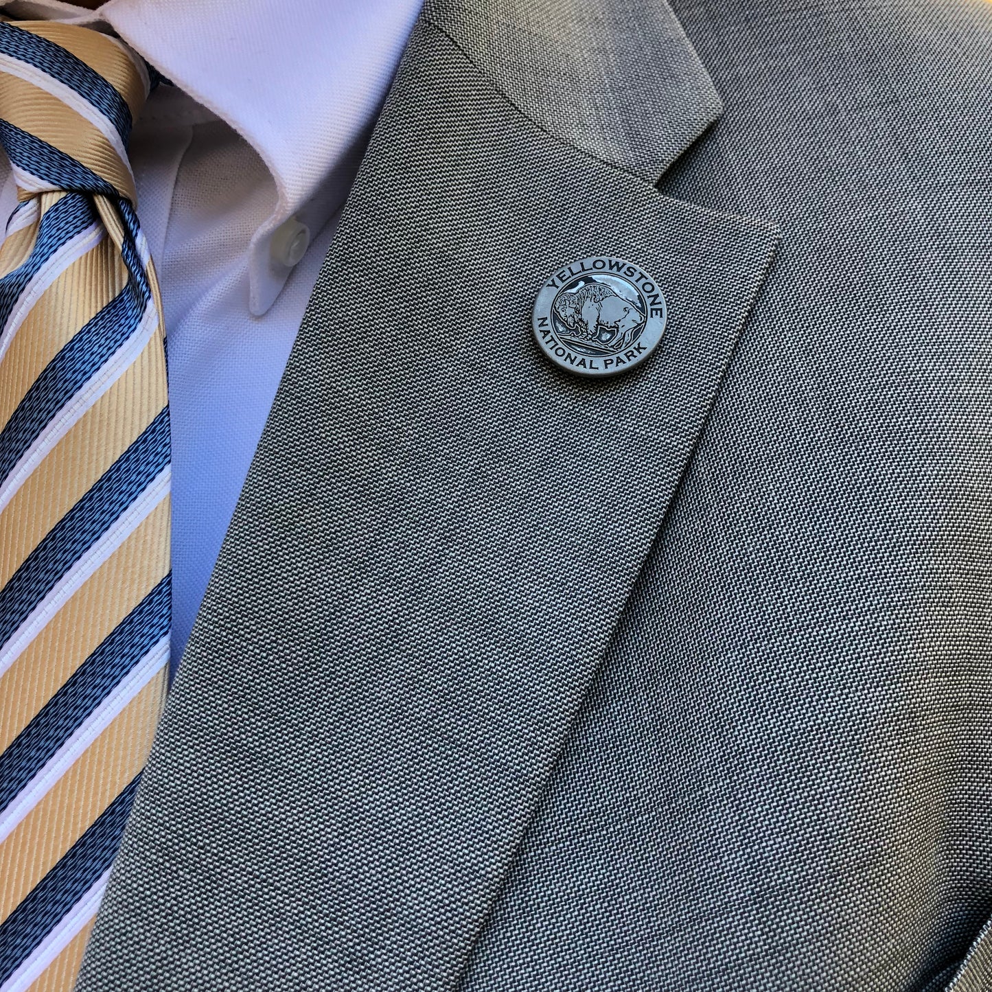 Gray suit jacket with a button featuring Yellowstone National Park logo, white shirt, and striped tie.