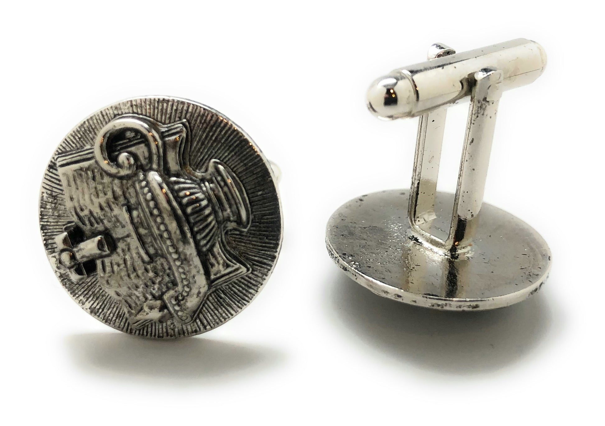 Silver cufflinks with detailed design on a white background