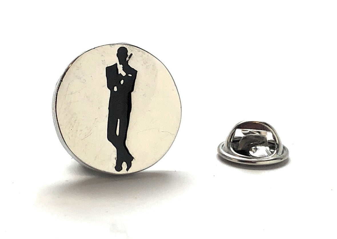 A silver and black enamel pin with a James Bond movie poster design, featuring a silhouette of a man in a suit with a cigarette.