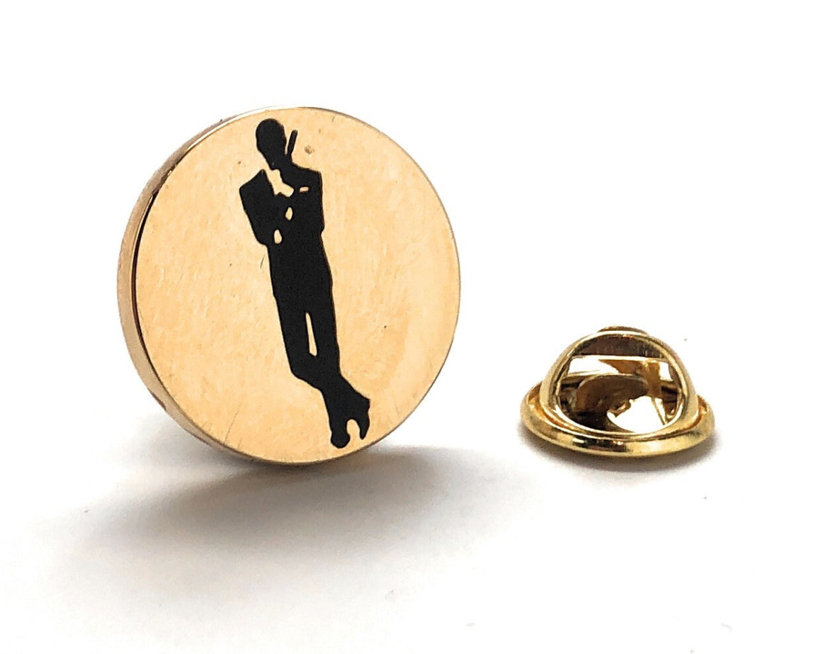 A gold and black enamel pin in the shape of a silhouette of a person wearing a tie, associated with the James Bond franchise.
