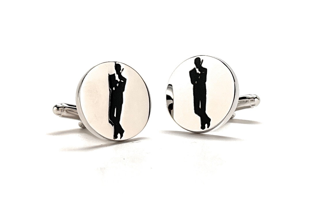 A pair of silver-colored cufflinks with an embossed design of a man in a suit, reflecting a movie poster pose.