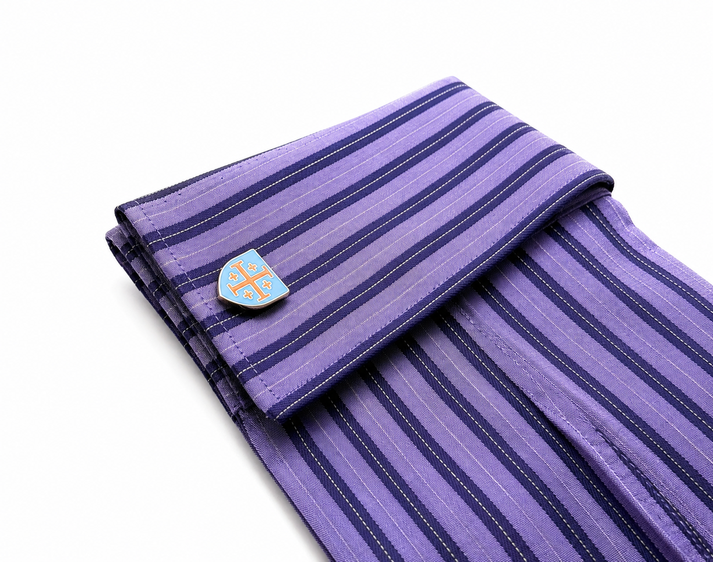 A folded purple striped necktie with a small shield-shaped cufflink featuring a gold cross on a light blue background, shown on a white background.