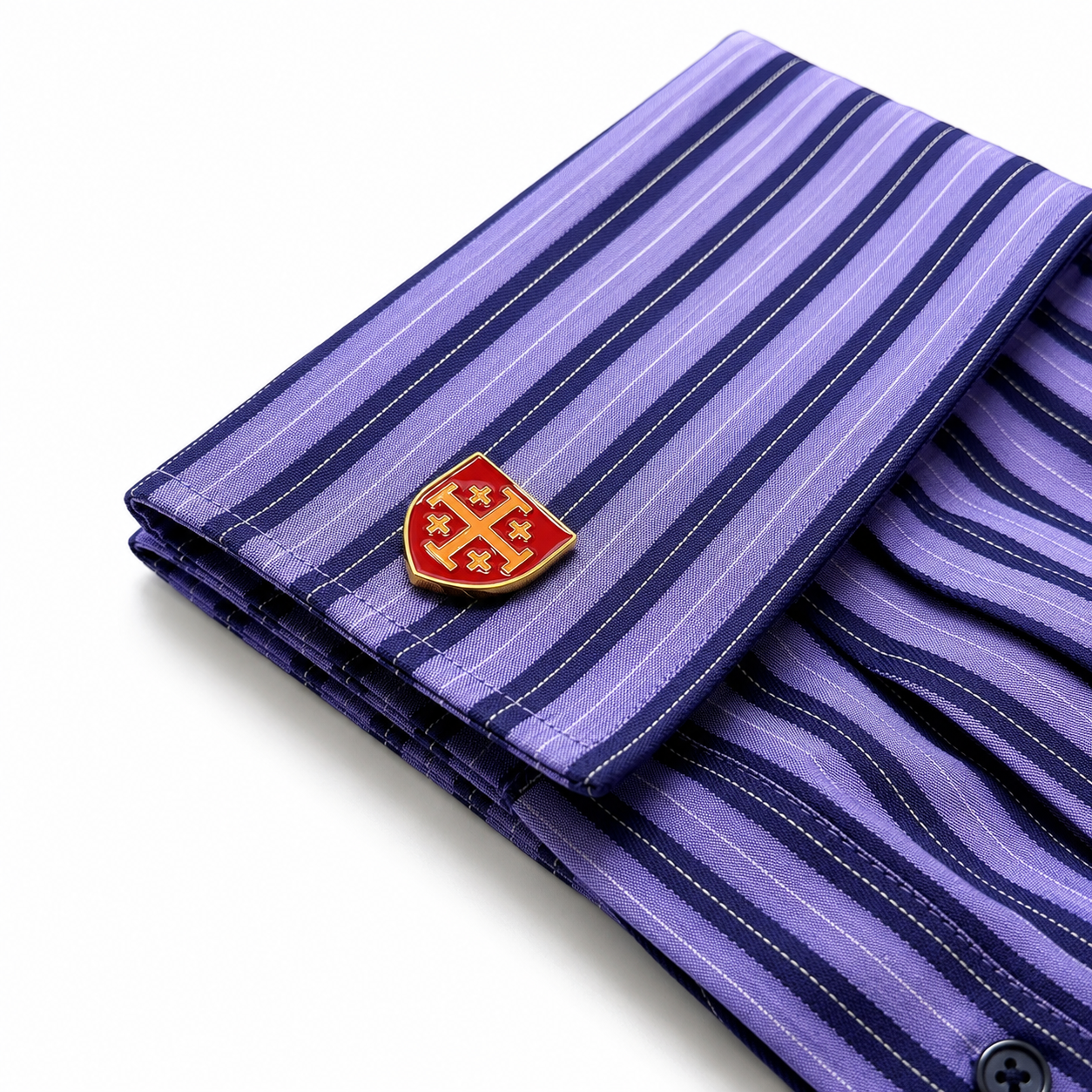 A folded purple striped dress shirt with a red and gold shield-shaped cufflink pin, shown on a clean white background. Luxury gold-tone Jerusalem Cross cufflinks