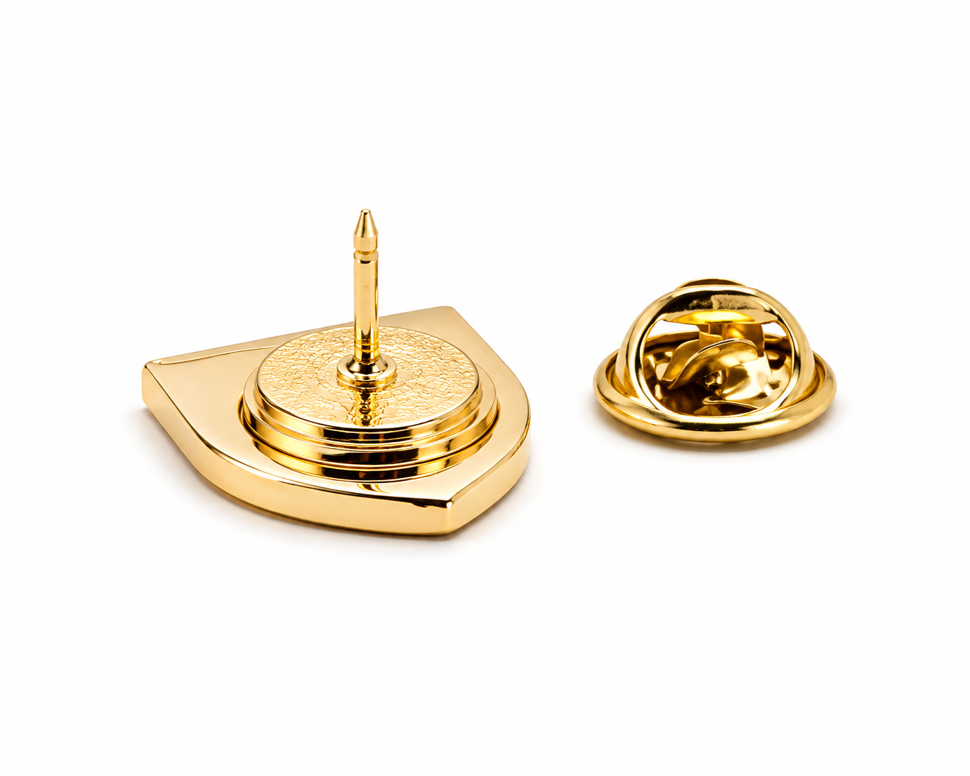 A gold-tone metal lapel pin shown from two angles on a clean white background: one view displays the front with a pointed pin and shield-like base, and the other shows the reverse side with the clasp mechanism.