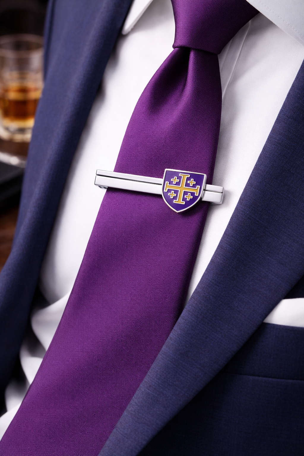 Purple tie with a Jerusalem Cross shield silver tie clip with purple and gold accents for men on a white shirt, close-up view.