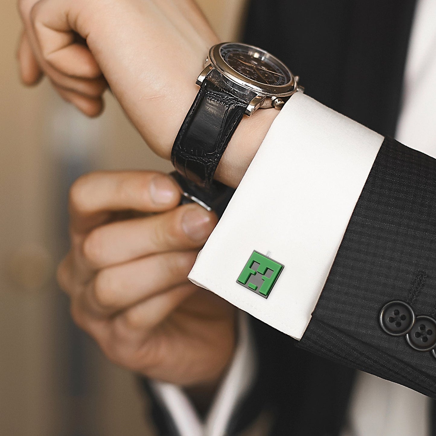 Close-up of a person wearing a watch with a unique cufflink featuring a green character.