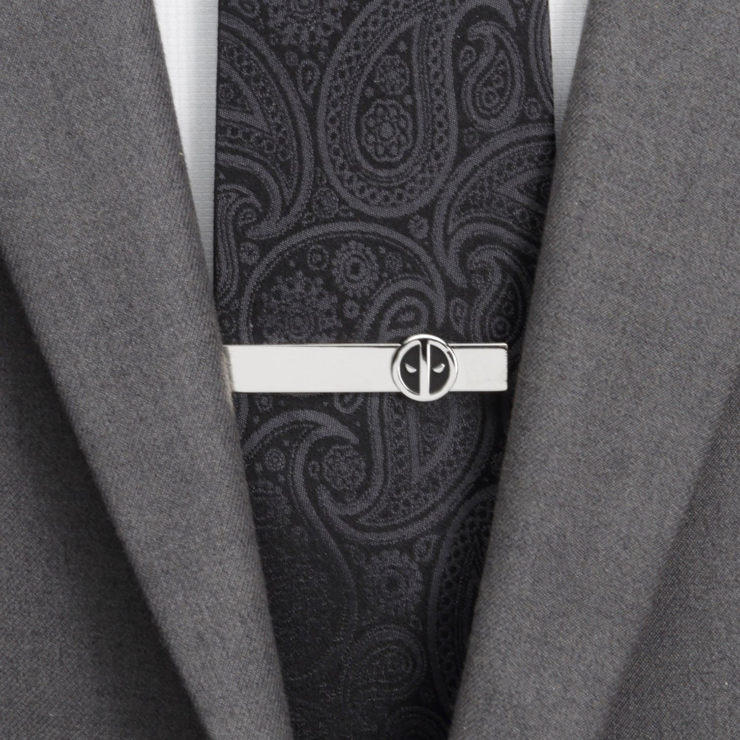 Black paisley tie with a silver tie clip on a gray suit jacket.