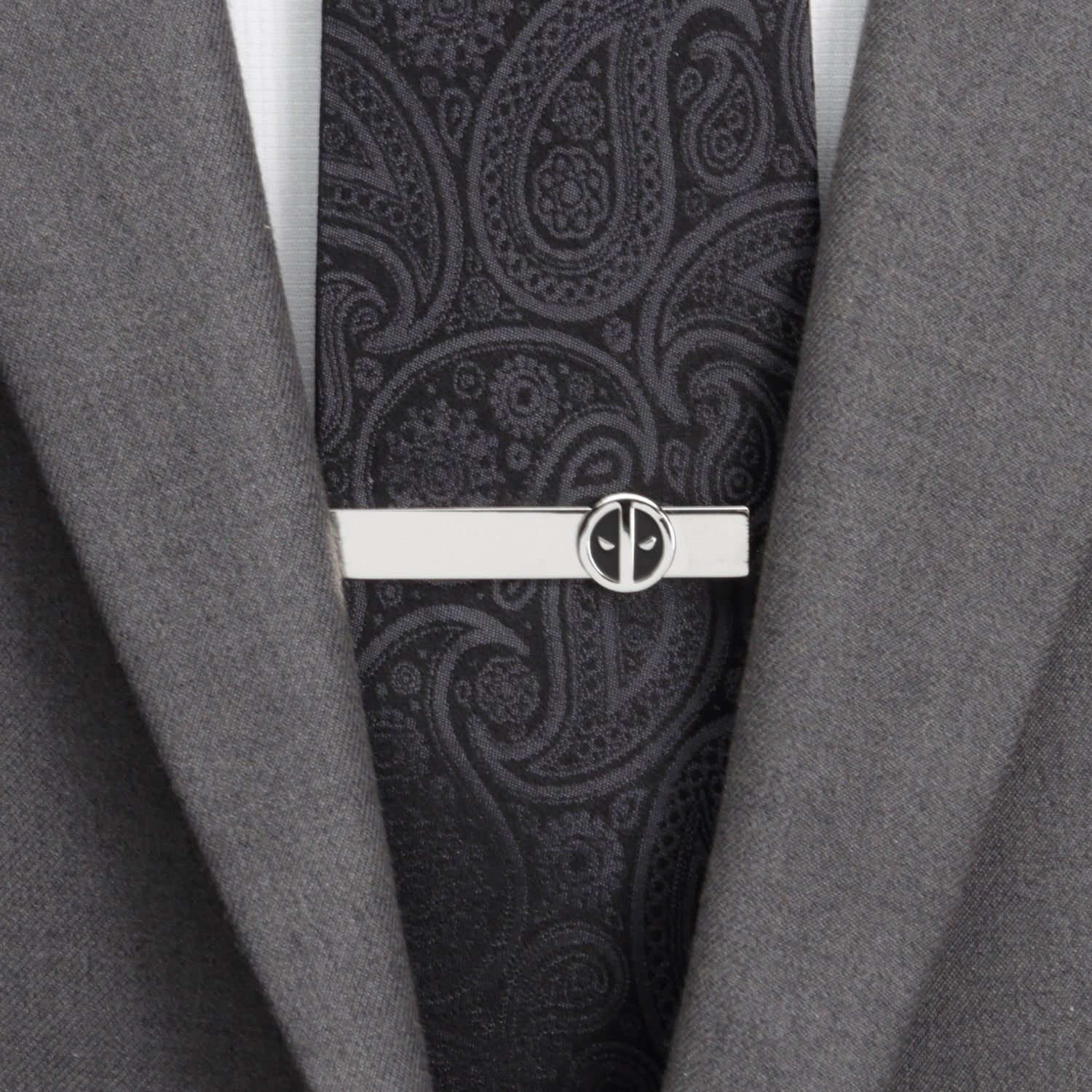 Black paisley tie with a silver tie clip on a gray suit jacket.