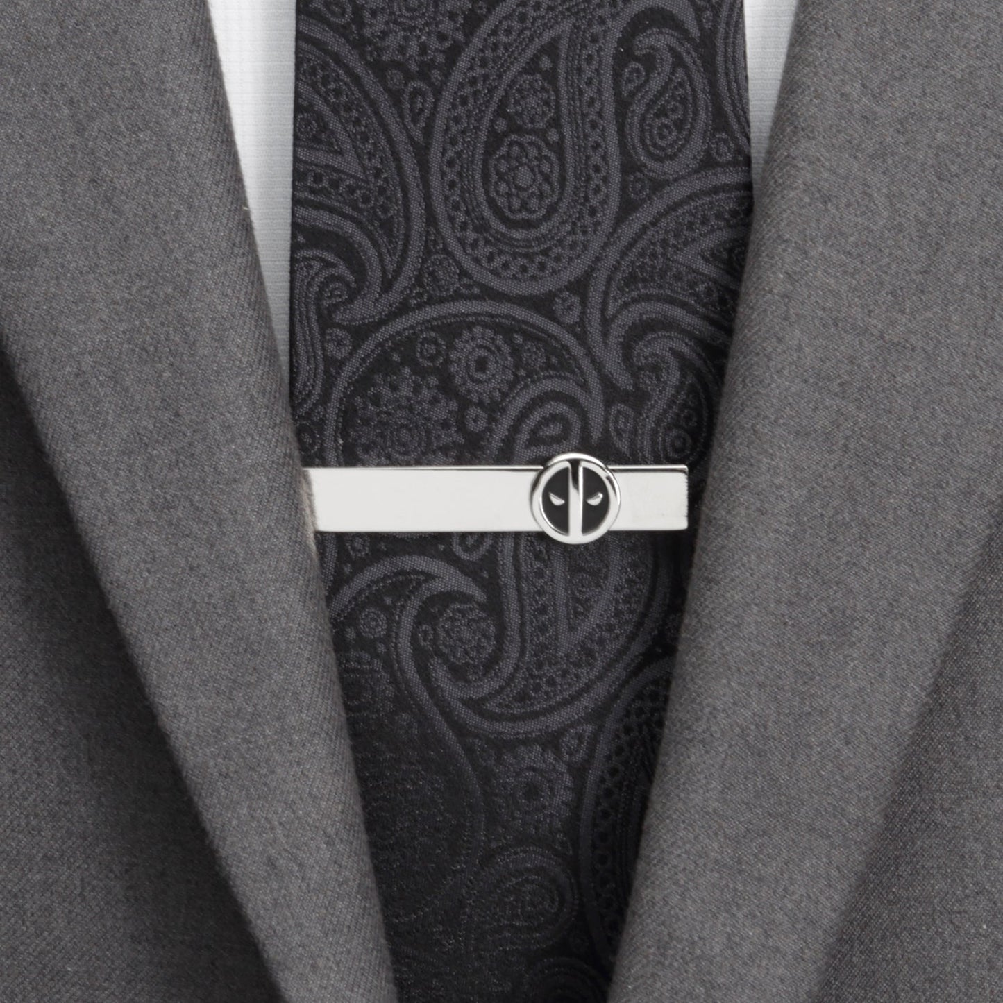 Black paisley tie with a silver tie clip on a gray suit jacket.