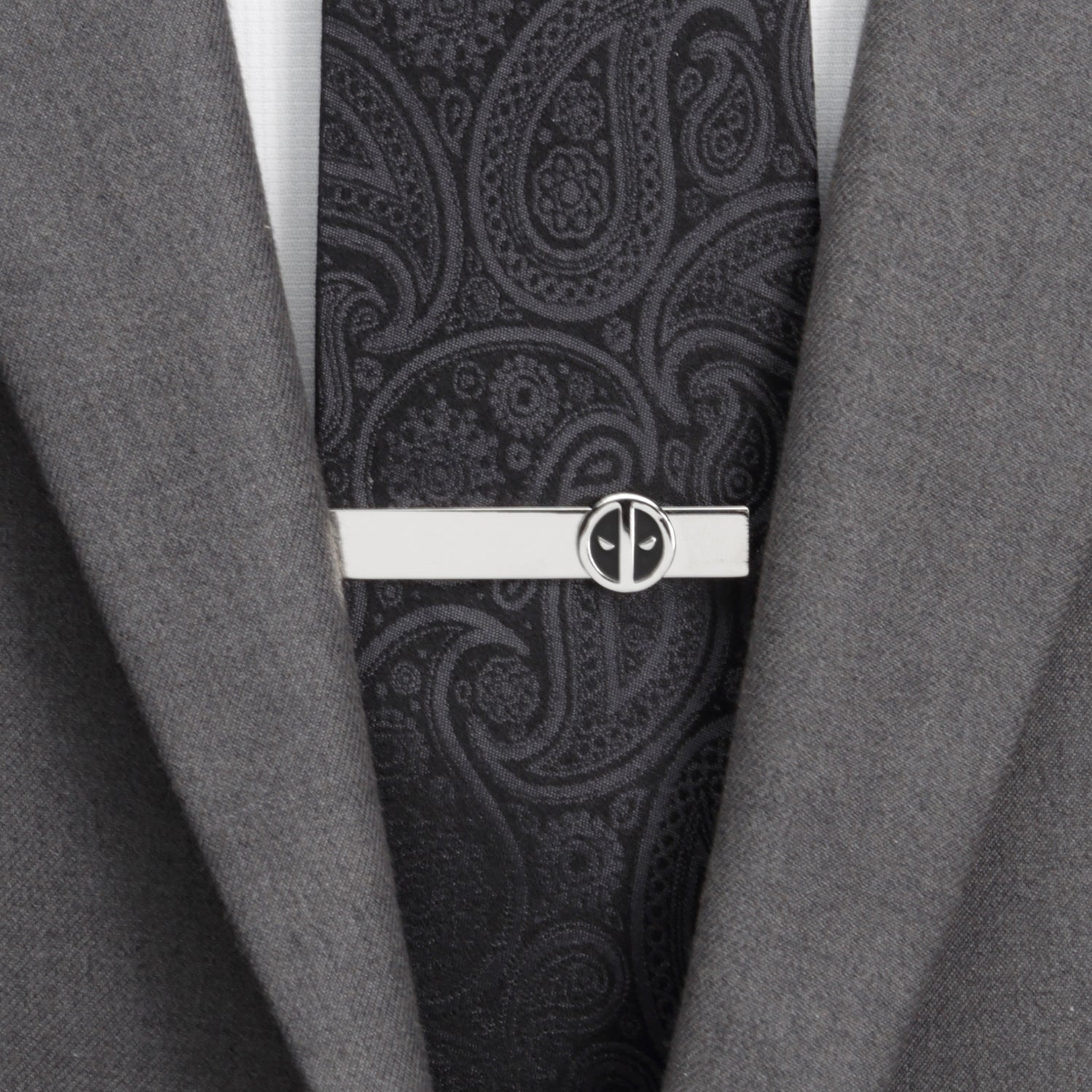 Black paisley tie with a silver tie clip on a gray suit jacket.