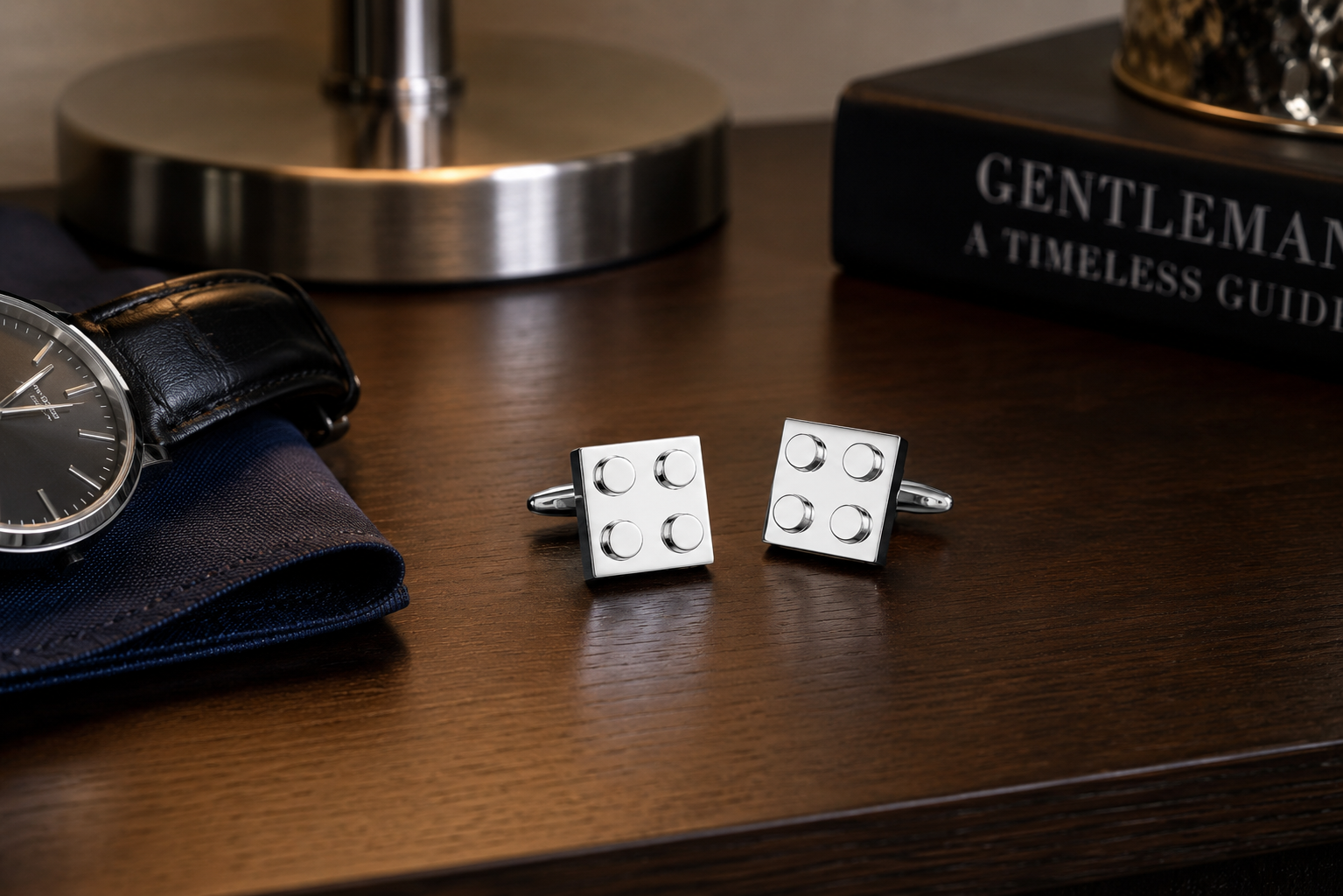 Silver cufflinks on a wooden surface with a watch and book in the background.