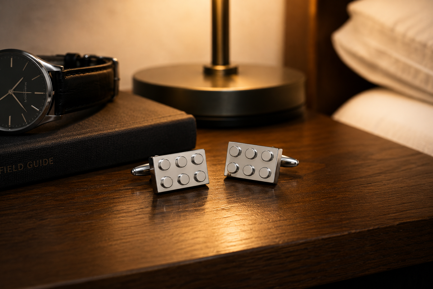 Silver building block cufflinks displayed on wooden nightstand beside watch and lamp