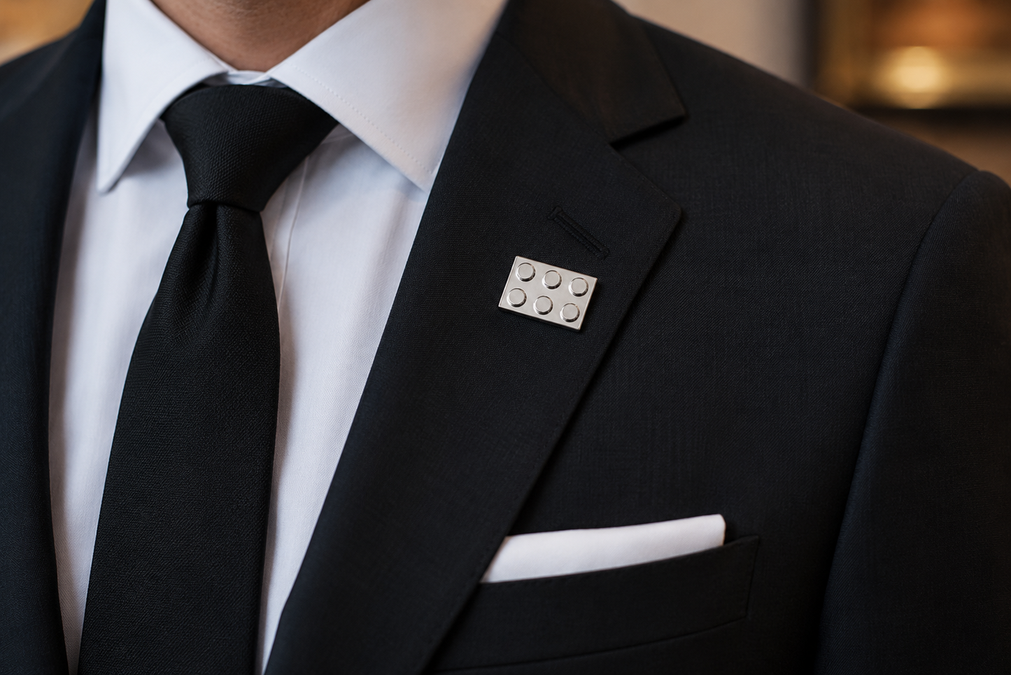 Silver building block lapel pin worn on a black suit jacket lapel