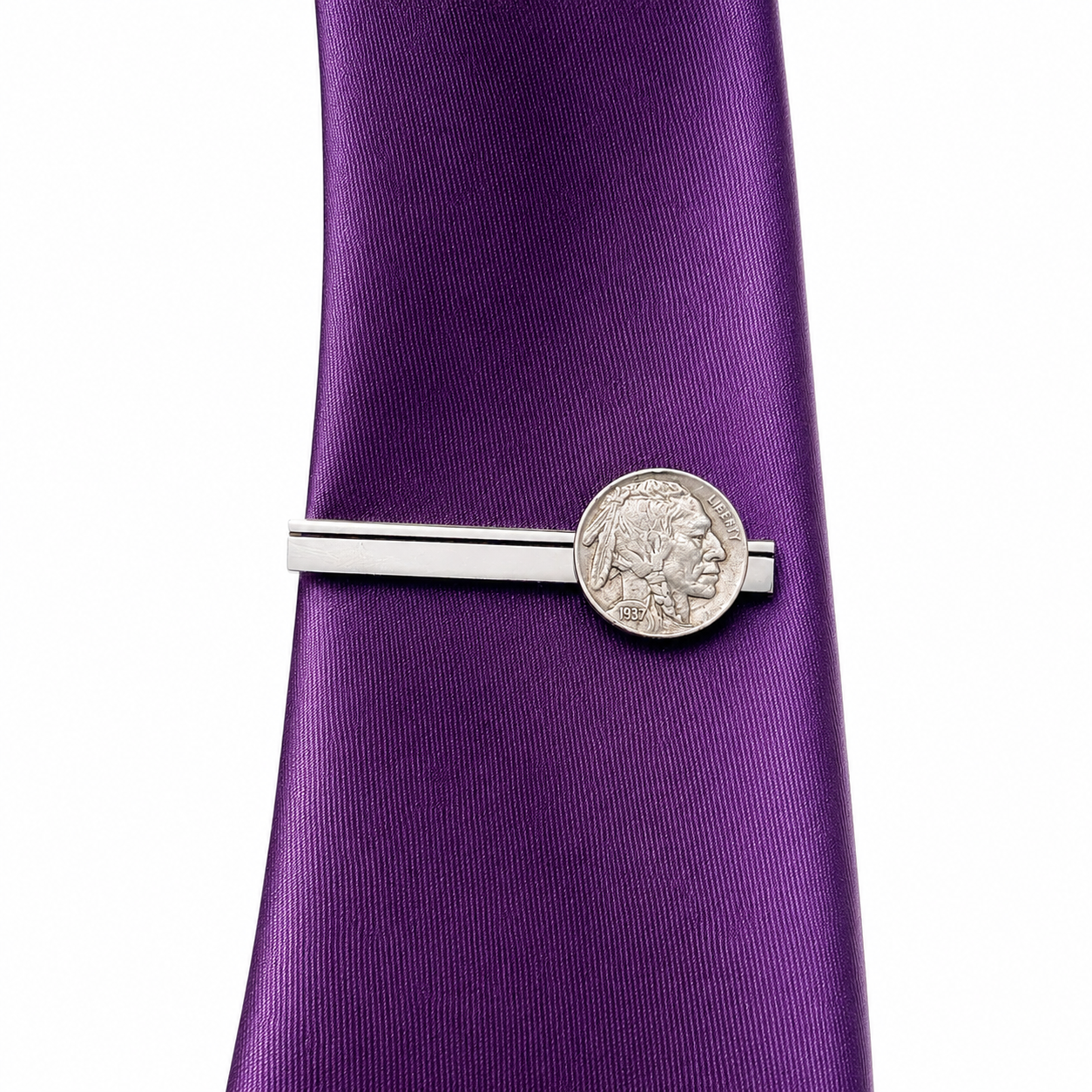 A silver tie bar with a circular Native American coin centerpiece, shown fastening a purple silk necktie against a plain white background.
