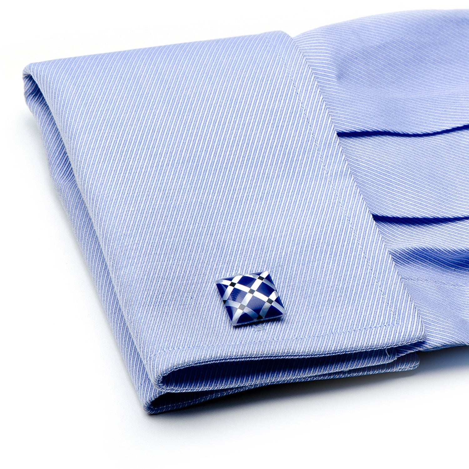 Folded light blue dress shirt with a decorative cufflink on a white background