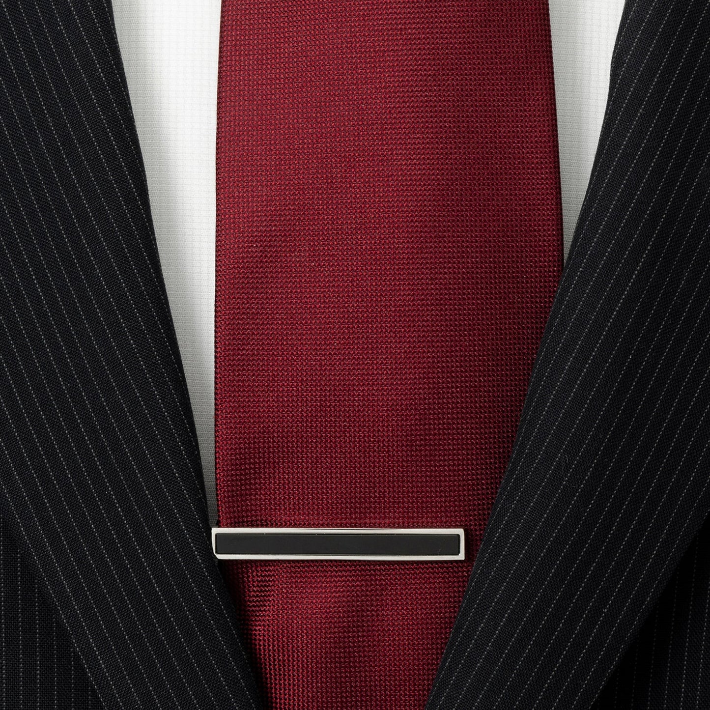 Maroon tie with a silver tie clip on a black pinstripe suit jacket.