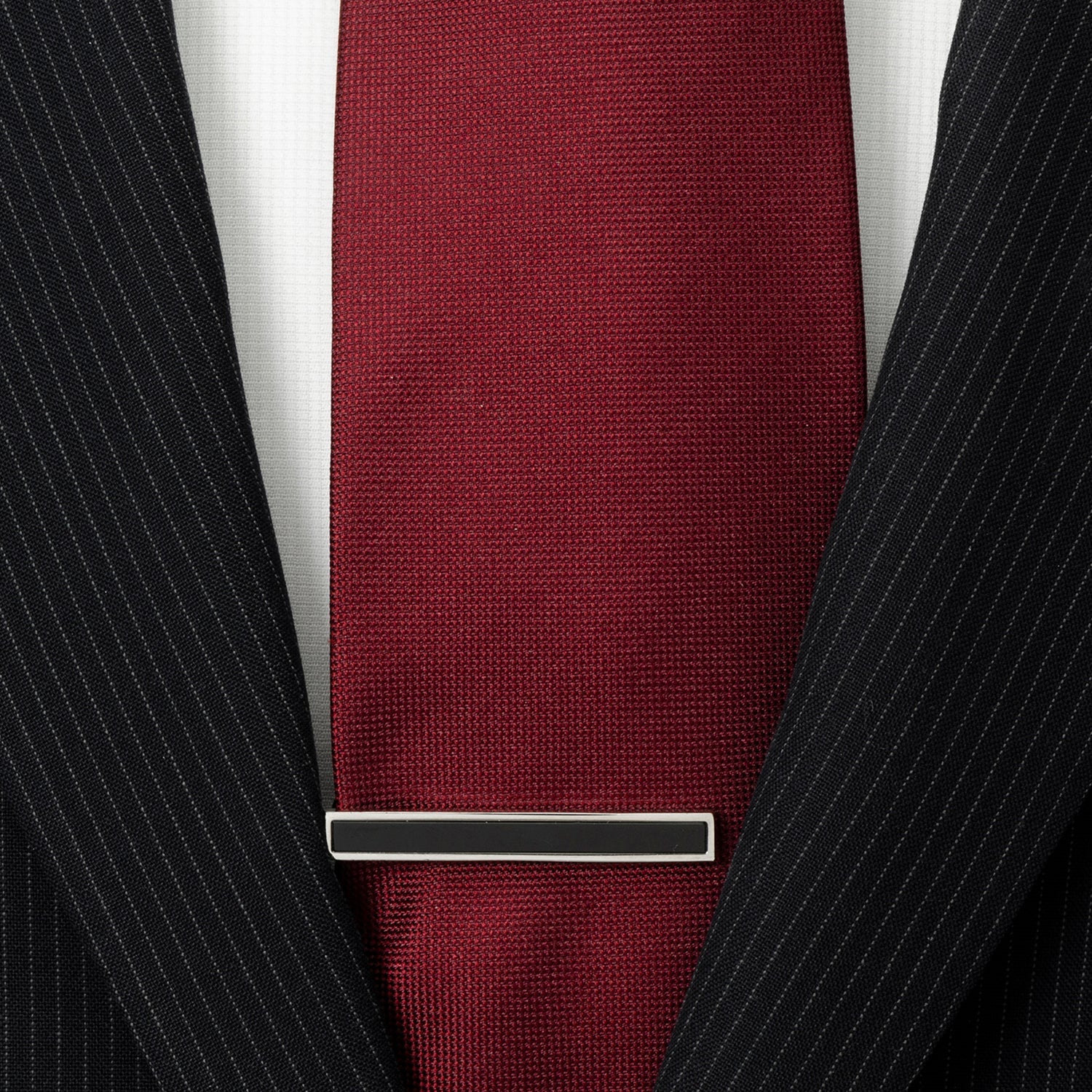 Maroon tie with a silver tie clip on a black pinstripe suit jacket.