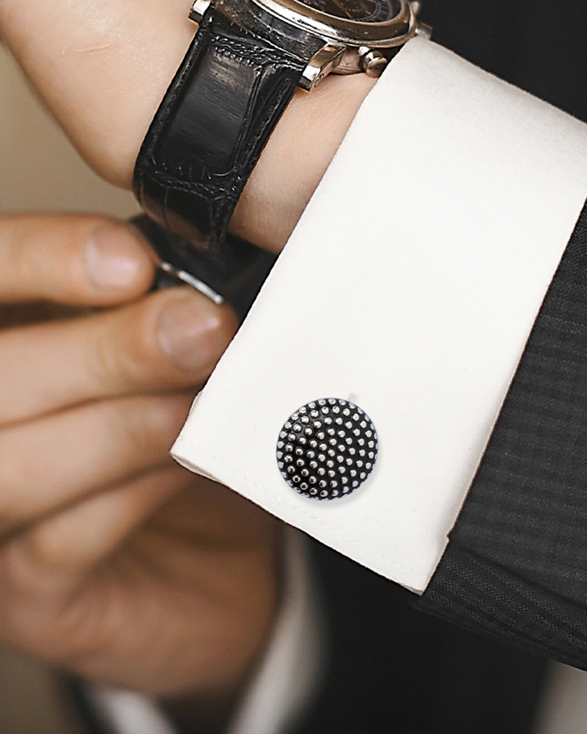 Close-up of a cufflink on a white cuff with a black leather watch.