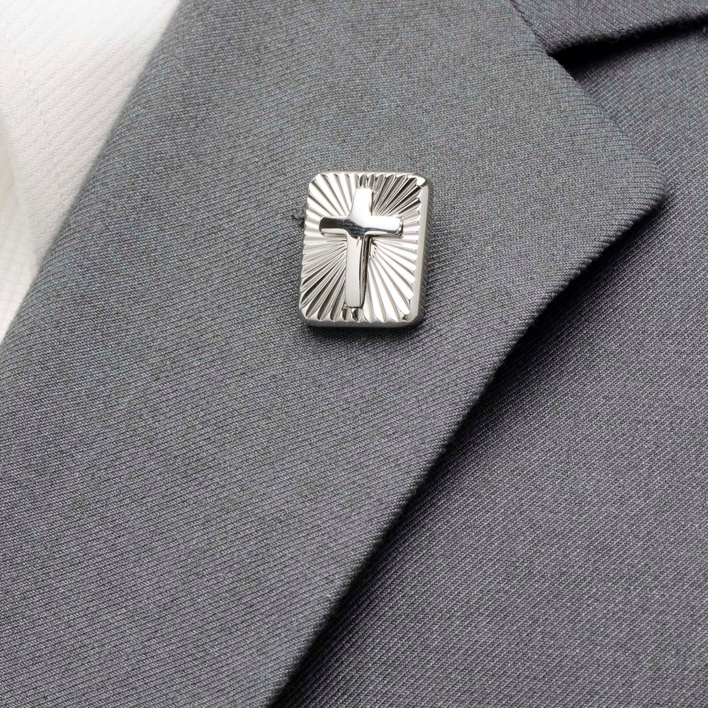 Silver cross lapel pin on a gray suit jacket